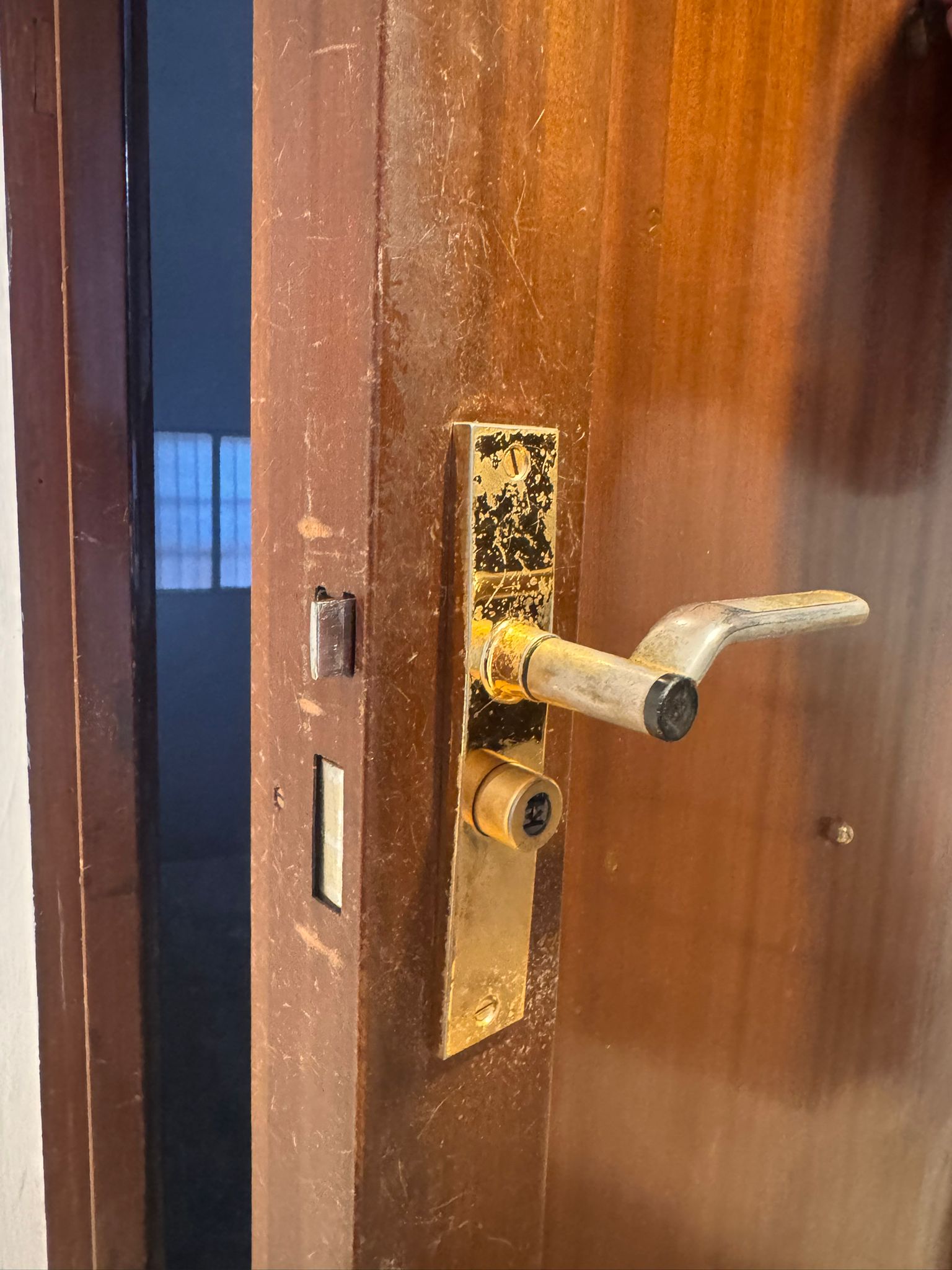 Cerradura antigua de latón oxidada con manilla de palanca desgastada en puerta de madera deteriorada
