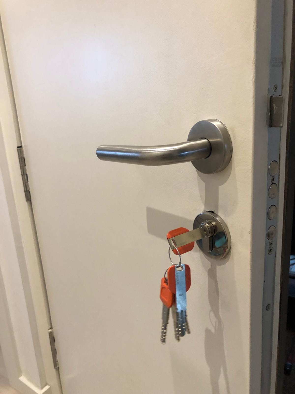 Puerta acorazada blanca con manilla de acero inoxidable y bombín con juego de llaves naranjas entregadas al cliente