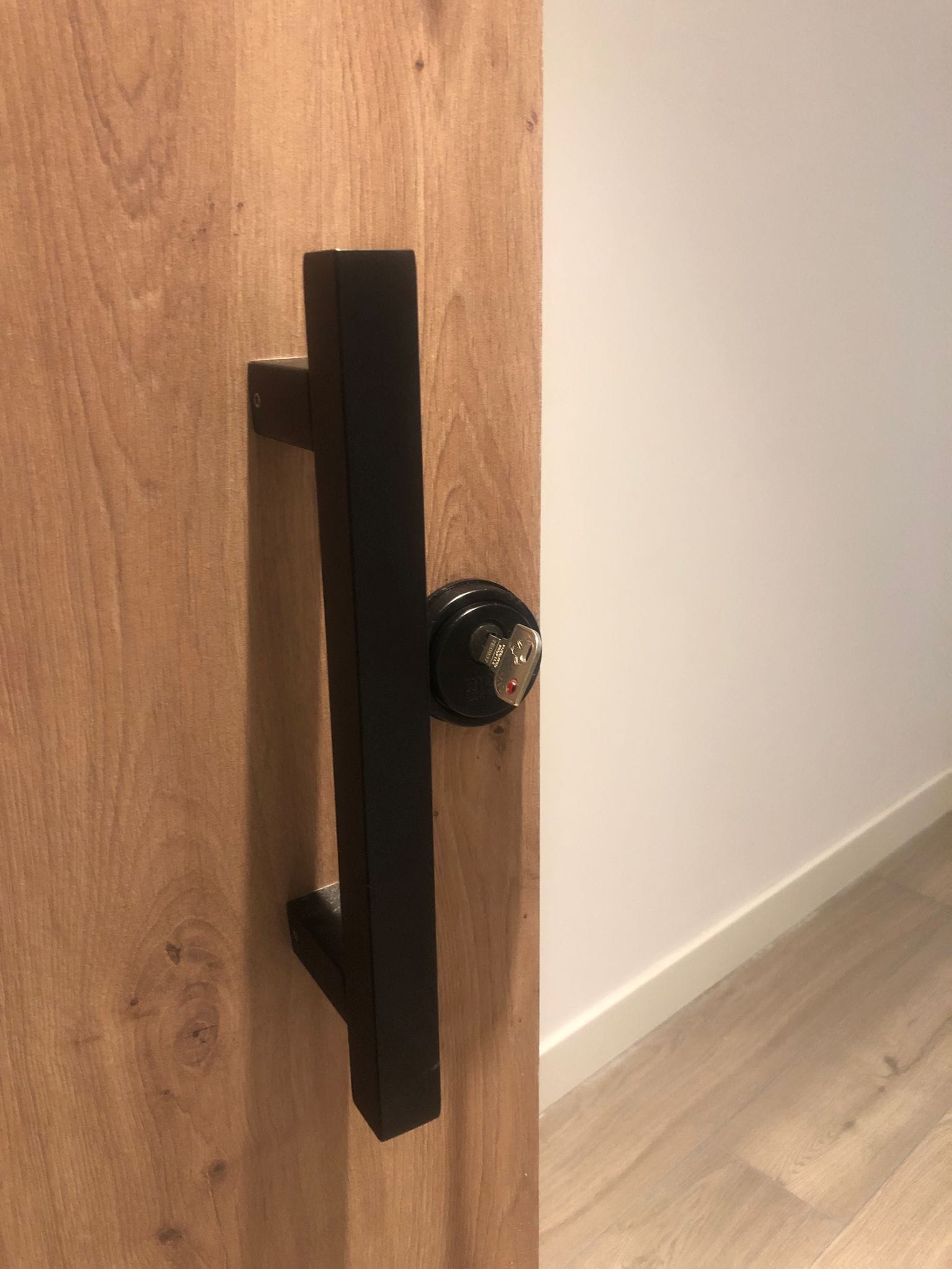Puerta corredera de madera con tirador negro mate y bombín de seguridad redondo instalado